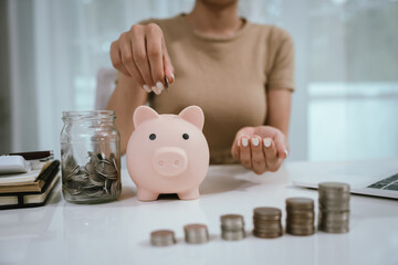 An Asian woman is writing in a notebook and stacking coins and a piggy bank, which symbolizes...