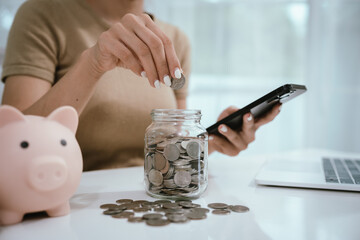 An Asian woman is writing in a notebook and stacking coins and a piggy bank, which symbolizes...