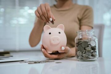 An Asian woman is writing in a notebook and stacking coins and a piggy bank, which symbolizes...