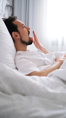 Young brunette man yawning and stretching after waking up in the morning