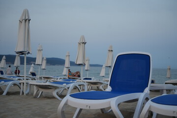 closed beach umbrellas and empty sun loungers on the coast of Golden Sands resort in Bulgaria, early morning or off-season, overcast sky and calm sea, tranquil beach scene
