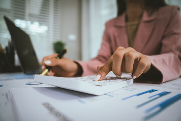 Fototapeta premium Businesswoman analyzing financial data using calculator, holding documents surrounded by charts, graphs and laptop, showing professionalism, business planning.
