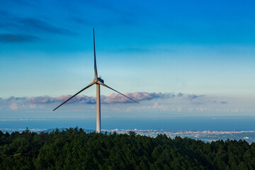 Single wind turbine on green hill with distant coastal city, Japan © GTPhoto