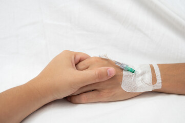 Close-up of hands holding each other, providing comfort and support to a patient with a medical cannula, highlighting empathy and care in a hospital setting