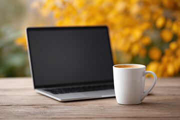 Laptop and coffee cup on wooden table with blurred yellow background create cozy autumn atmosphere