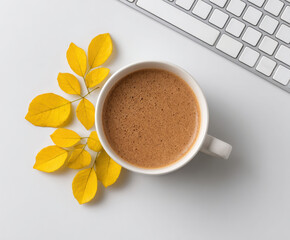 Warm cinnamon drink in white mug sits beside yellow leaves and keyboard on white desk