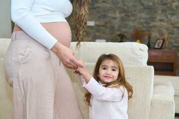 Pregnant mother holding hands with her daughter at home