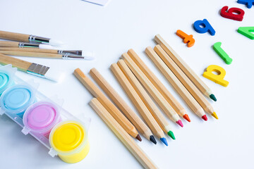 Colorful art supplies with brushes, pencils, and magnetic letters on white background