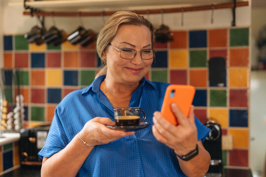 Woman enjoys coffee while using smartphone in a colorful kitchen setting during the morning