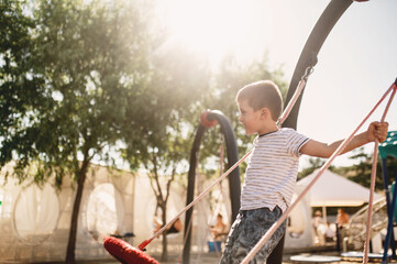 Preschool boy swinging on swing on beach against backdrop of holiday bungalow summer mood