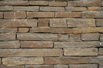 Natural sandstone wall texture with irregular horizontal layers and warm earthy tones. Rough stacked stone surface ideal for architectural backgrounds and 3D materials.