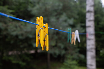 Close-up of colorful plastic clothespins hanging on a blue clothesline outdoors, with a soft focus forest background. A simple summer moment captured in natural light.