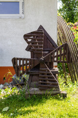 Small decorative wooden windmill in garden near house wall on green grass.