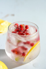 Glass filled with summer cocktail made with lemon slices, redcurrants, and ice cubes.