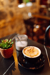 Close-up of a cup of aromatic cappuccino with a cupcake stands on a wooden table in the rays of the sunset. A delicious hot drink with dessert in a coffee shop. Food and drink concept.