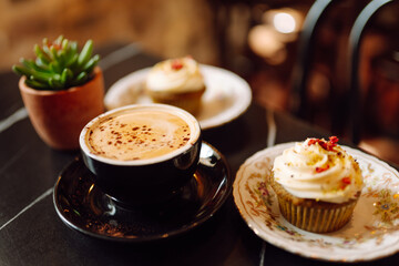 Close-up of a cup of aromatic cappuccino with a cupcake stands on a wooden table in the rays of the sunset. A delicious hot drink with dessert in a coffee shop. Food and drink concept.