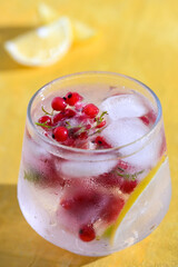 Glass filled with summer cocktail made with lemon slices, redcurrants, and ice cubes.