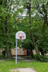 Basketball hoop with white backboard and net on outdoor court surrounded by green trees.