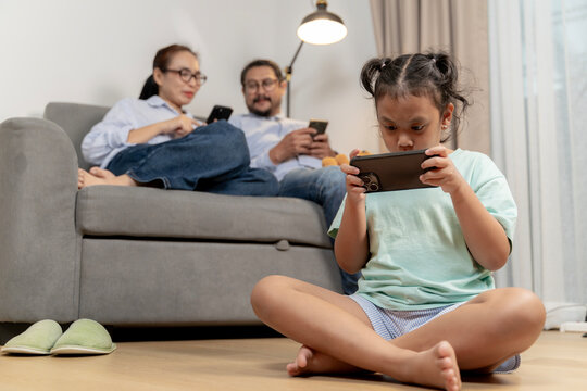 A father, mother, and young daughter each focused on their smartphones, reflecting modern digital habits and reduced family interaction.