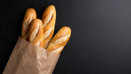 Four golden brown baguettes are partially visible inside of a tan paper bag, set against a dark background.