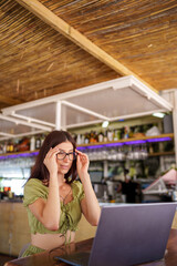Professional woman working remotely, wearing glasses and using laptop at urban cafe bar