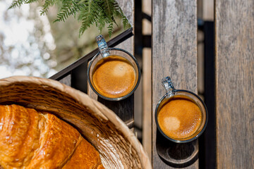 deux tasses de café crémeux posées sur une table de jardin vue de dessus avec des croissants et...