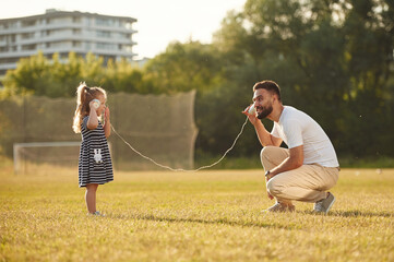Tin can telephone fun. Father with his little daughter are on the field
