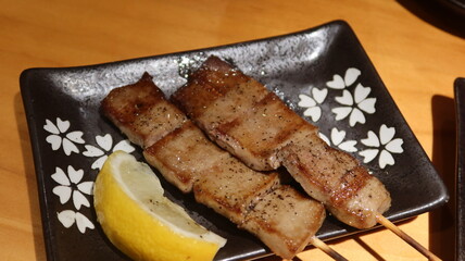 close up of two Japanese grilled ox tongue skewers on a black plate with copy space in a izakaya with lemon slice
