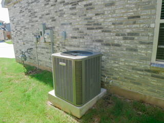 Top view fan of AC condenser unit with blades, casing, and placement, concrete pad with ductwork and electrical conduit enter the house, grassy yard, brick siding new home in Princeton, Texas