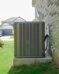 Visible duct connections, electrical lines and refrigerant tubing of outdoor AC unit on concrete pad, clean siding brick wall of new house in Princeton Texas. HVAC setup, AC installation concept
