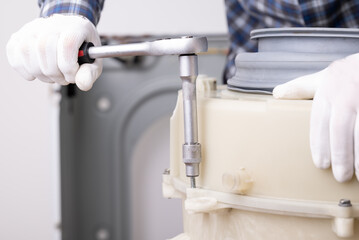 Tightening washing machine screw during repair. Hands in white gloves tighten a washing machine screw with a socket wrench, step in assembly