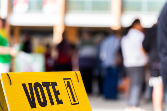 vote 1 on sign with out of focus voters waiting to enter polling station