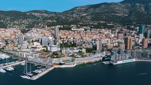 Glamorous drone panorama of Monaco&rsquo;s Larvotto coast: luxury super‑yachts, Casino de Monte‑Carlo domes, high‑rise skyline and sheer Maritime Alps plunging into the sapphire Mediterranean Sea.
