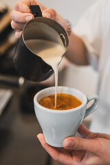 Close-up of a barista pouring steamed milk into espresso to create a latte, showcasing coffee preparation and creamy texture in a cafe setting.