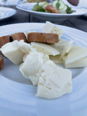 Plate with assorted white cheese and sliced bread with olives, served on rustic wooden table