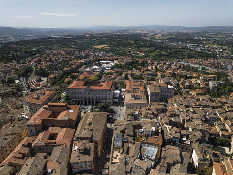 Aerial view of terracotta rooftops cascading across the ancient cityscape, punctuated by the grandeur of historic buildings like the Palazzo dei Priori, Perugia, Umbria, Italy.