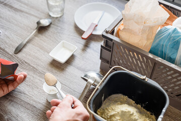 Man making bread at home kitchen adding ingredients to the dough. Baking bread at home with flour, dough, and yeast, preparing in a bread maker with a mold