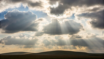 Dramatic sky with sunbeams shining through the clouds over a rolling landscape