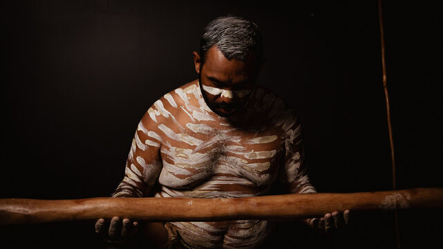 Aboriginal male looking down at didgeridoo