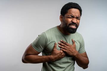 Young man feeling sudden chest pain, possible heart attack symptoms, touching chest in studio on isolated background