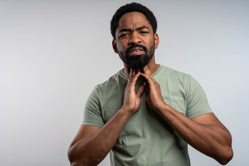 Sick young man touching his sore throat in pain, studio portrait of ill person on isolated background