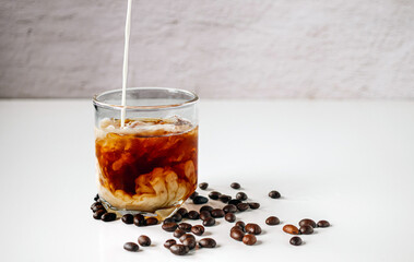 Latte coffee, Milk pouring from a milk jug into a glass of iced coffee with coffee beans on a white background