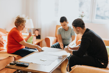 Fototapeta premium A family bonding indoors, playing cards and spending quality time with warm sunlight streaming through the windows. Emphasizes leisure, togetherness, and a comfortable atmosphere.