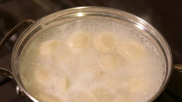 Cooking dumplings in boiling water and skimming foam. Dumplings boiling in pot on gas stove as foam is skimmed with spoon, symbol of care and homemade food