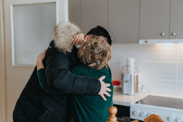 A touching scene of an elderly lady sharing a warm hug with a loved one inside a modern kitchen,...