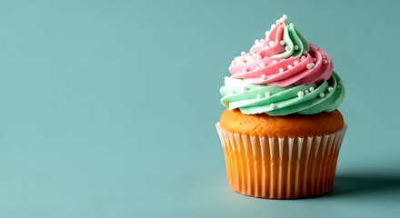 Single cupcake with pink and green frosting and white sprinkles on a teal background icing sweet