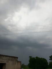 Dramatic storm clouds gather over rural landscape, promising rain and casting a moody atmosphere on the distant trees and fields, evoking a sense of anticipation and natural power