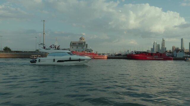 Luxury yacht cruising near fire rescue boats at the Chicago marina during golden hour.
