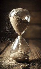Close-up of hourglass with flowing golden sand on rustic wooden table, warm side lighting creating dramatic shadows, time management and patience concept with copy space.