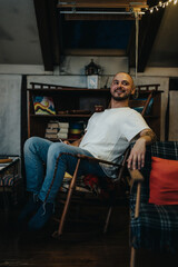 A cheerful man casually sitting on a chair in a warmly decorated indoor setting, surrounded by comfortable furniture and enjoyed atmosphere. The scene conveys comfort, warmth, and relaxation.